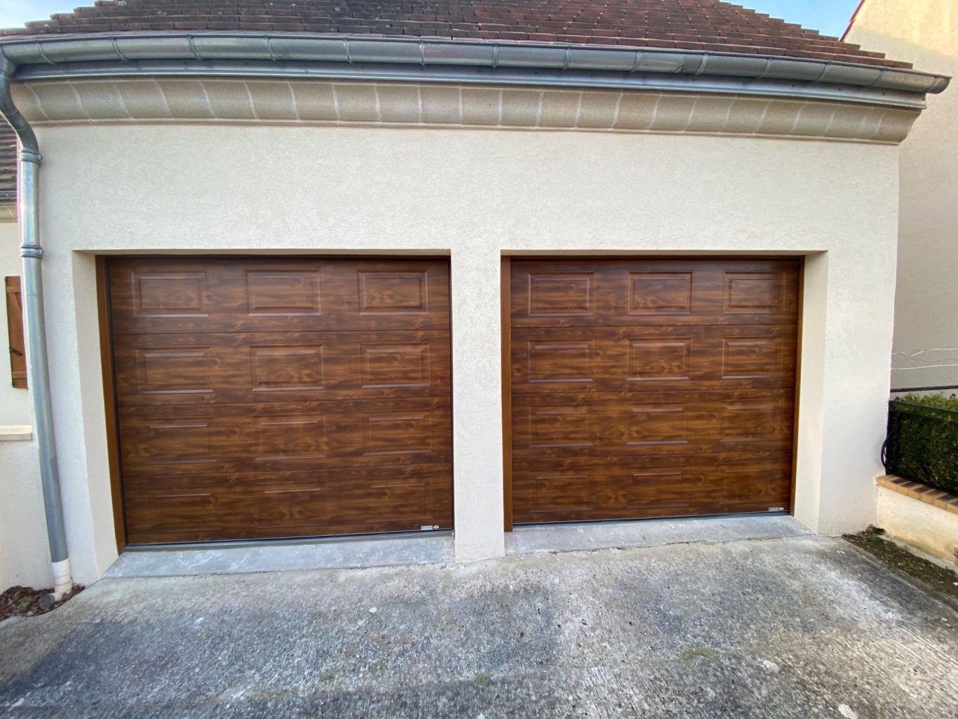 Deux portes de garage en bois avec finition brune, situées sur un mur clair.