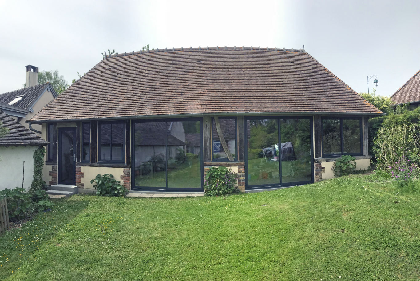 Maison avec véranda vitrée sur un jardin verdoyant. Toit en tuiles.