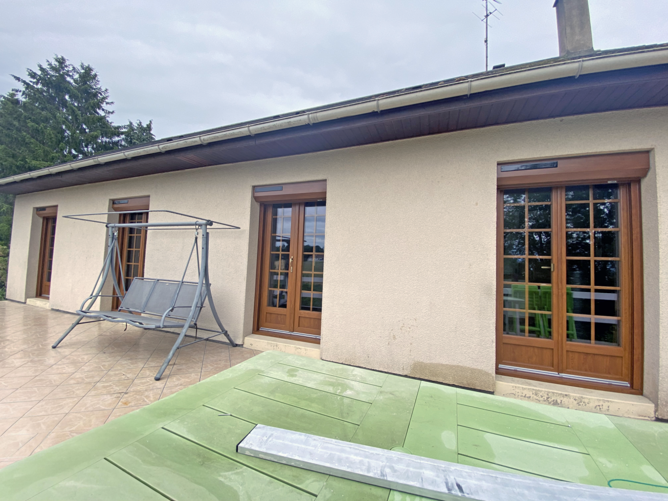 Maison avec fenêtres à battants, balançoires et jardin en arrière-plan.