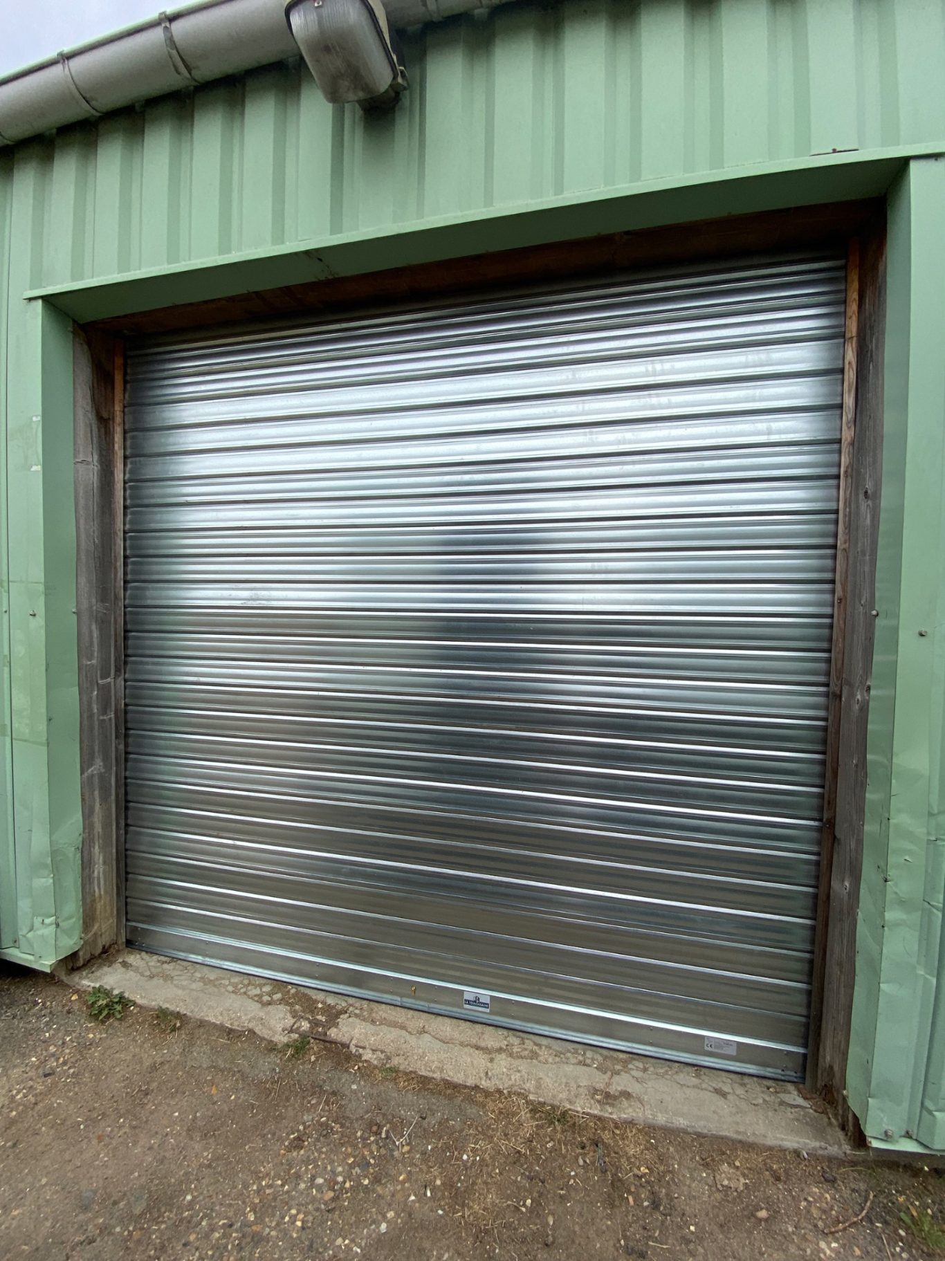 Porte de garage en métal roulant avec un cadre en bois, sur un mur vert.