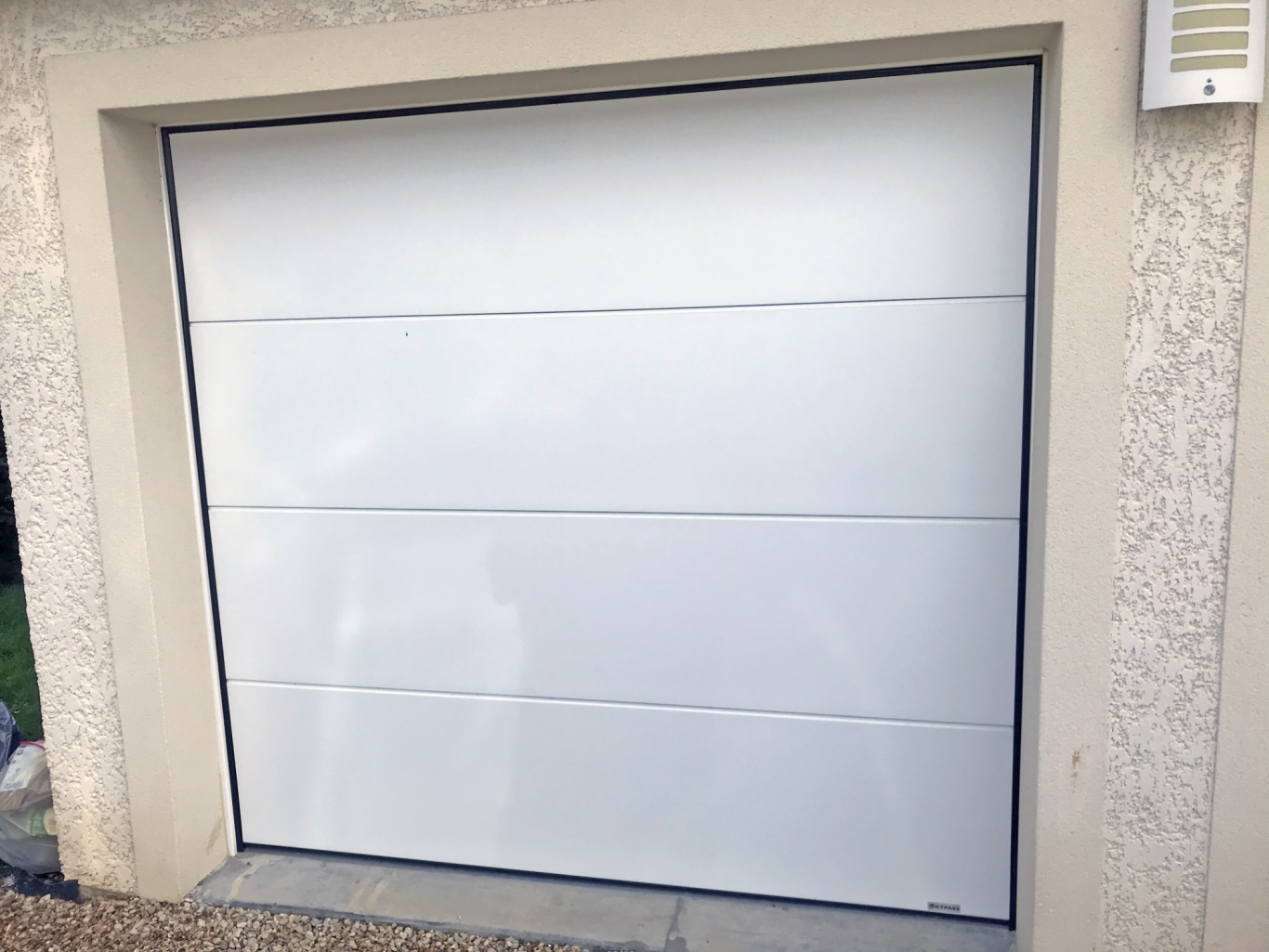 Portail de garage blanc avec des panneaux lisses, installé dans un mur beige.