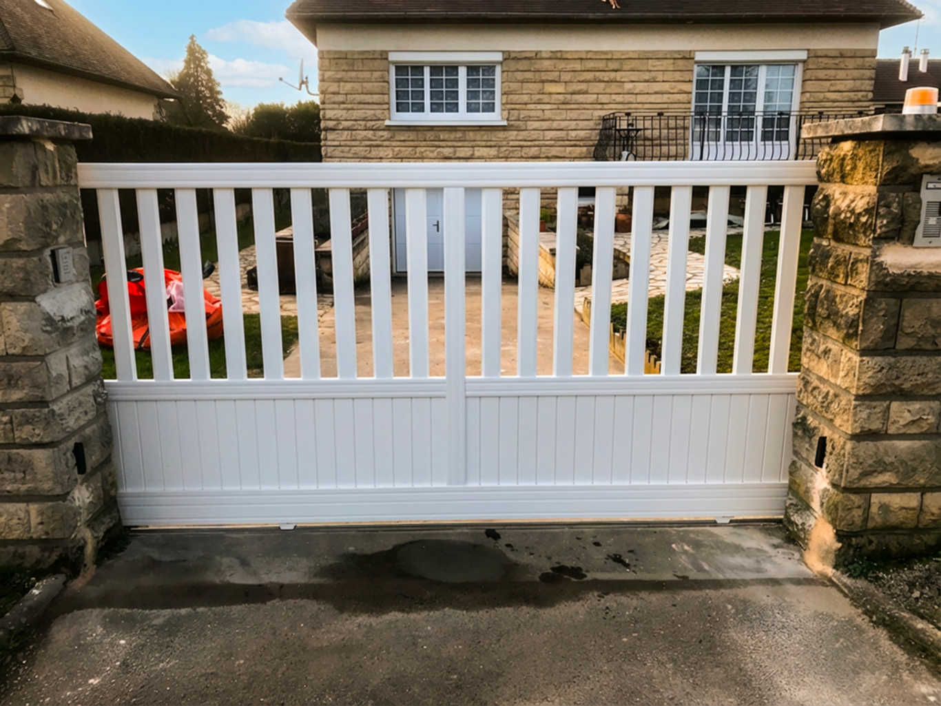 Portail en bois blanc avec des panneaux verticaux, devant une maison en pierre.