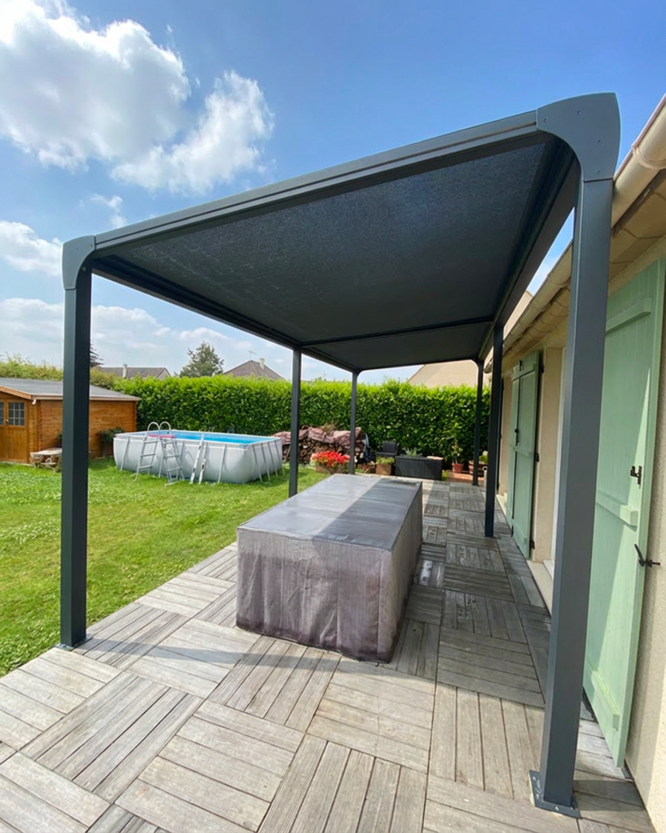 Auvent moderne en métal au-dessus d'une table sur une terrasse gazonnée.