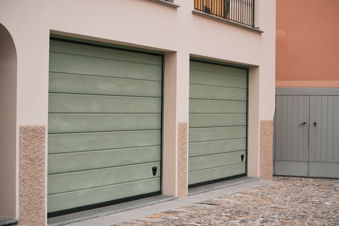 Deux portes de garage vert pâle encadrées par un mur beige et un mur rosé.