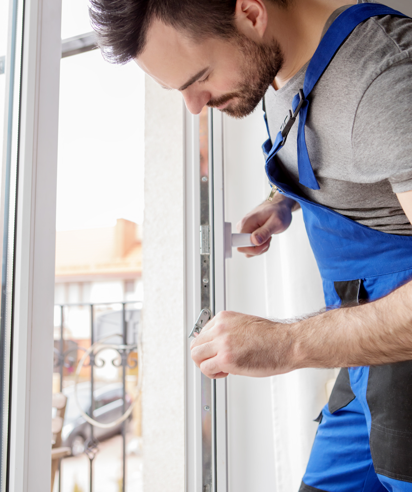 Homme en salopette réparant une fenêtre avec un outil à la main.
